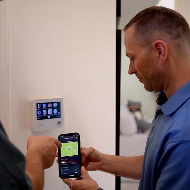 McElroy's residential HVAC technician helps a homeowner to link their mobile phone to their smart thermostat.