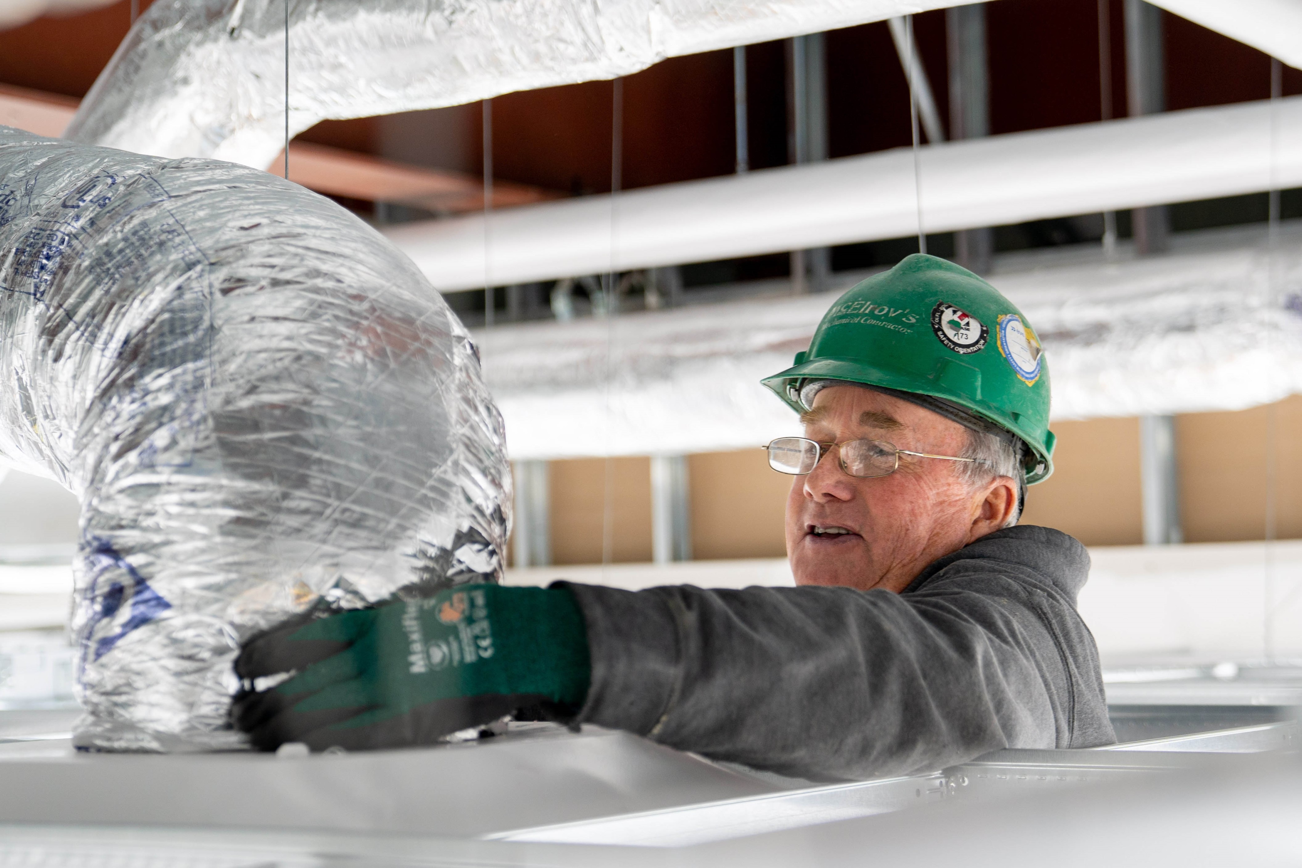 McElroy’s commercial construction sheet-metal foreman, Gail Sage, places flexible ductwork above a ceiling.