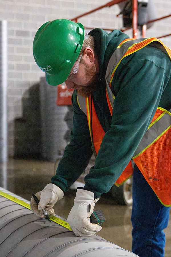 McElroy’s commercial construction sheet-metal foreman, Tanner Darveaux, measures a length of circular air duct.