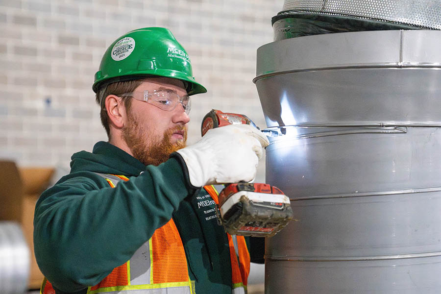 McElroy’s commercial construction sheet-metal foreman, Tanner Darveaux, fastens a reducer on top of a large, circular air duct.